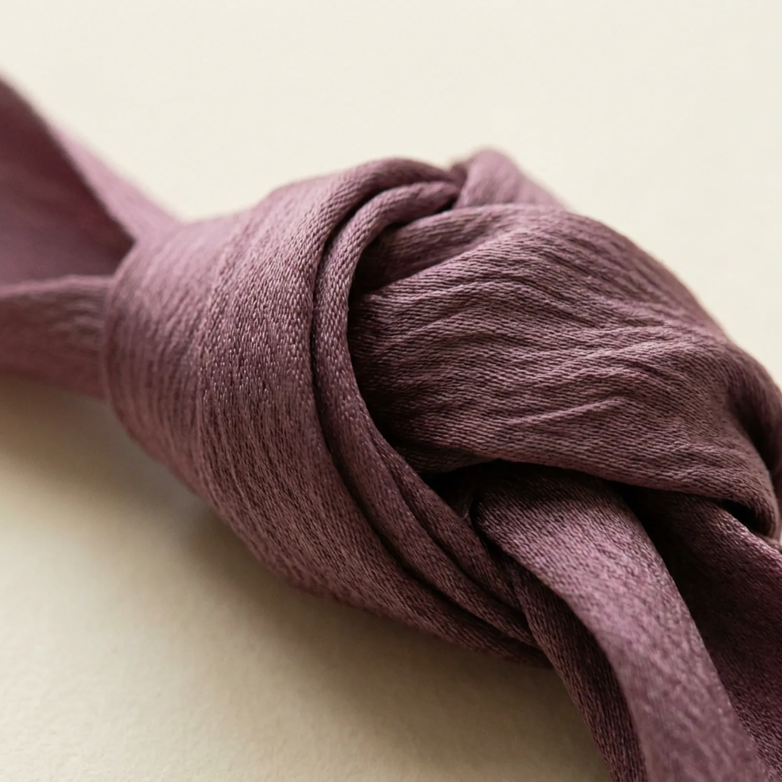 Extreme close-up of a knot of plum silk ribbon, the weave of the fabric filling the frame in soft raking light.
